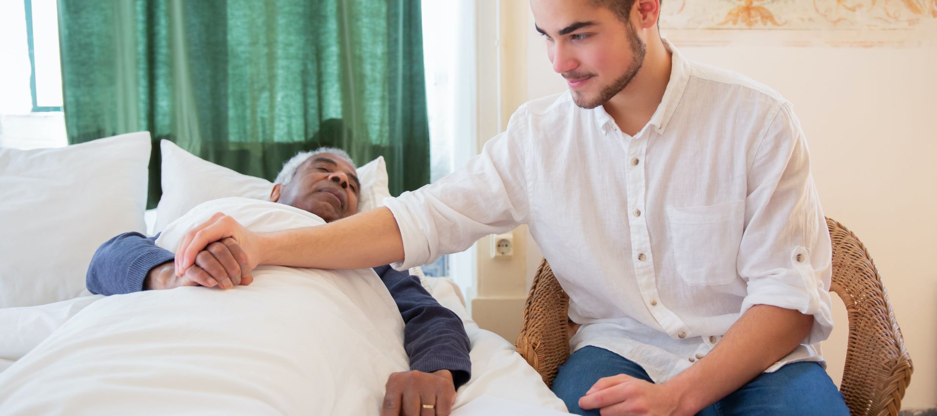 Man in White Button Up Shirt Sitting Beside Elderly Man in Bed